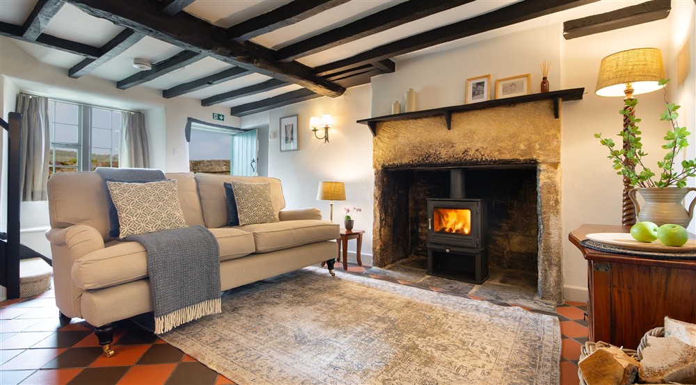 The open-plan sitting and dining room with sofa, woodburner and original beams at Barn Owl Loft in Itteringham, Norfolk