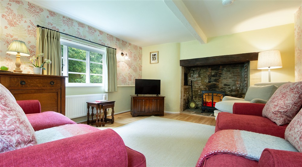 The sitting room with sofas, armchair, television and original inglenook at Beech Cottage in Bridport, Dorset