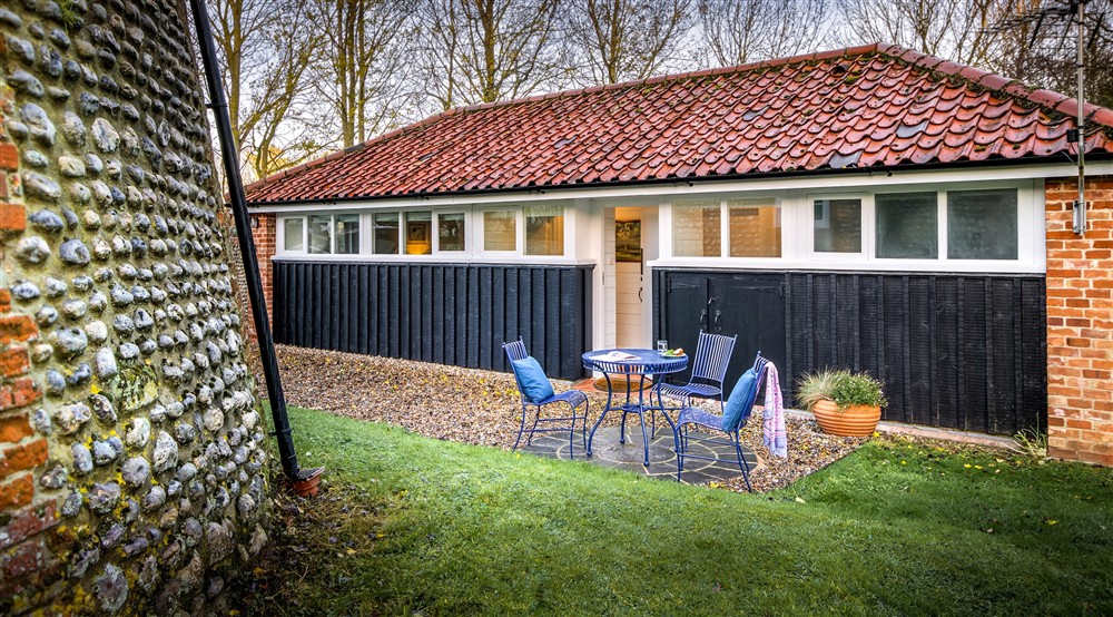 The exterior of Blakeney Lodge and its walled garden, with a patio with outdoor dining furniture, a lawn and the base of the windmill, Norfolk at Blakeney Lodge in Blakeney, Norfolk