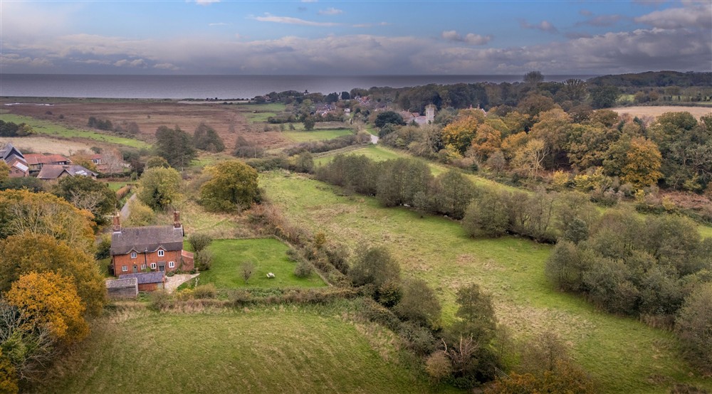 An aerial view of Bridge Farm Cottage in autumn, with the Dunwich village and the sea in the distance, Suffolk