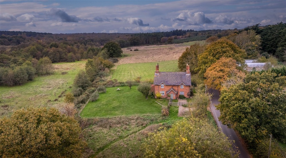 An aerial view of Bridge Farm Cottage on the right and the adjoining cottage on the left, surrounded by fields and woodland, Suffolk