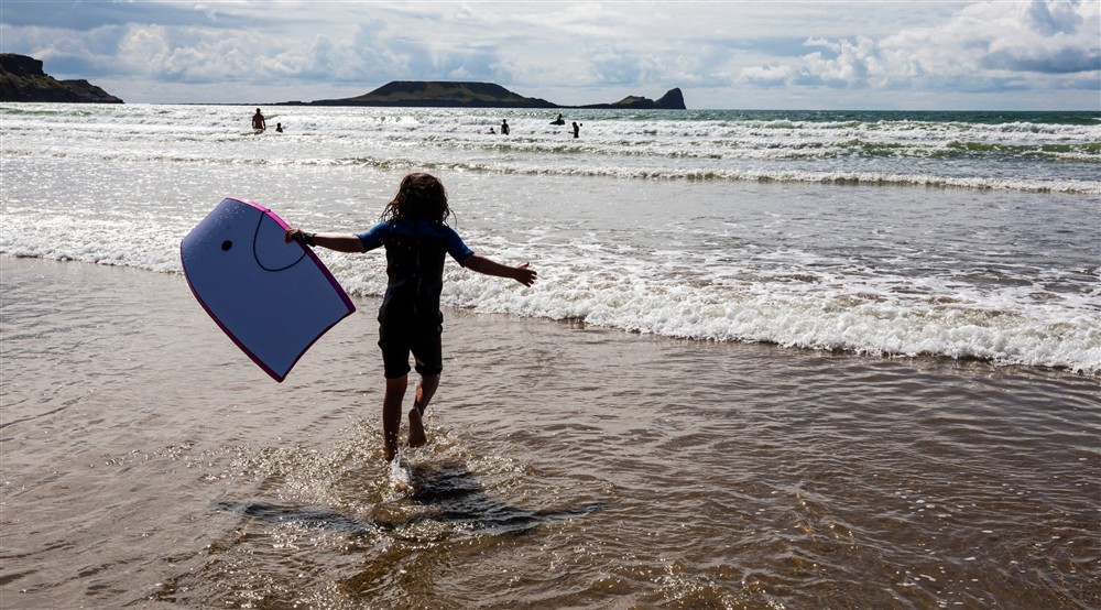 The silhouette of a child running into the sea with a bodyboard at Burrows Cottage in Swansea, South Wales