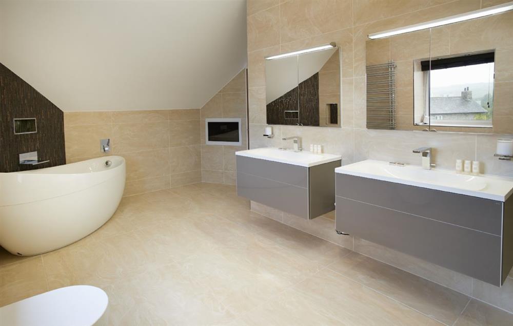 En-suite bathroom with waterfall shower, his & hers sinks, spa bath and built-in wall TV at Carus House, Burneside