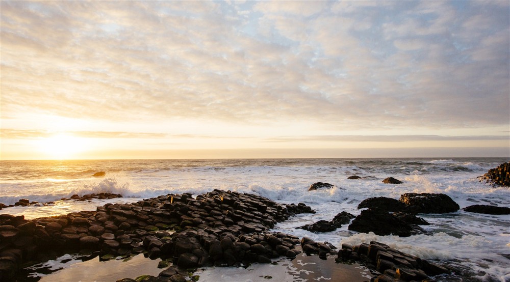 Waves breaking over a rocky coastline as the sun sets on the horizon at Castle Ward Bunkhouse in Downpatrick, County Down