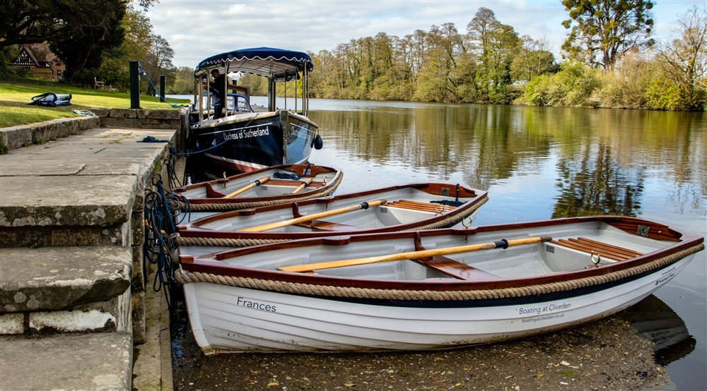 An image of boats resting on the smooth surface of the water on the River Thames, surrounded by trees and greenery at Cliveden New Cottage in Nr Maidenhead, Berkshire