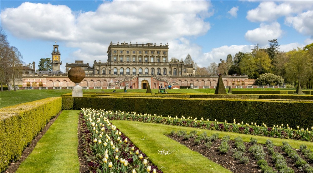 Low-level view of spring borders with a grand manor house beyond at Cliveden New Cottage in Nr Maidenhead, Berkshire