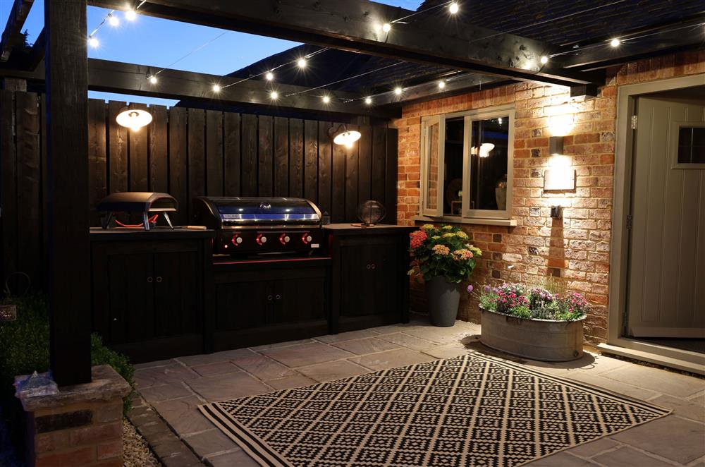The outdoor kitchen is lit with cosy lighting in the evening  at Coach House, Walton, Near Stratford-upon-Avon
