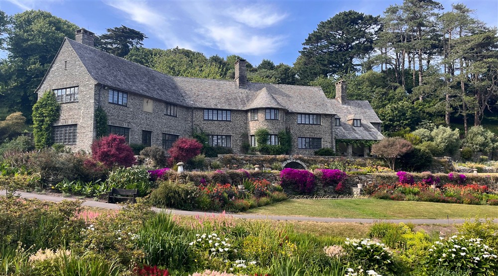 Stone house sits facing a green lawn with bright purple, red and white flowers in borders on a sunny day (photo 2) at Compass Cottage in Dartmouth, Devon