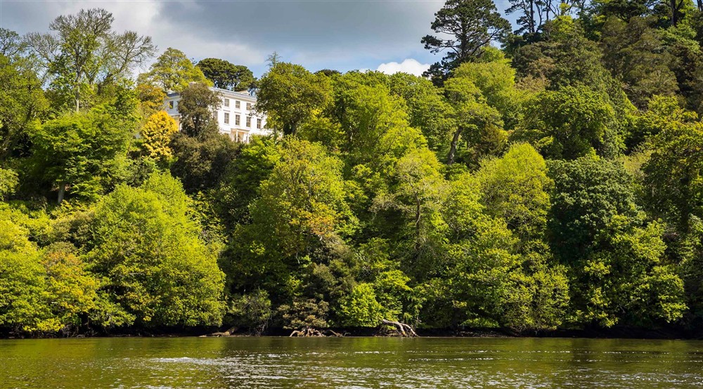 The River Dart is in the foreground with a tree-lined riverbank behind and Greenway House seen through the trees high on the hill in the background. at Compass Cottage in Dartmouth, Devon