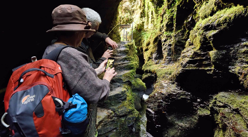 Visitors taking photos with mobile phones on the viewing platform of the Devils Cauldron at Cotehele Engine Cottage in Calstock, Cornwall