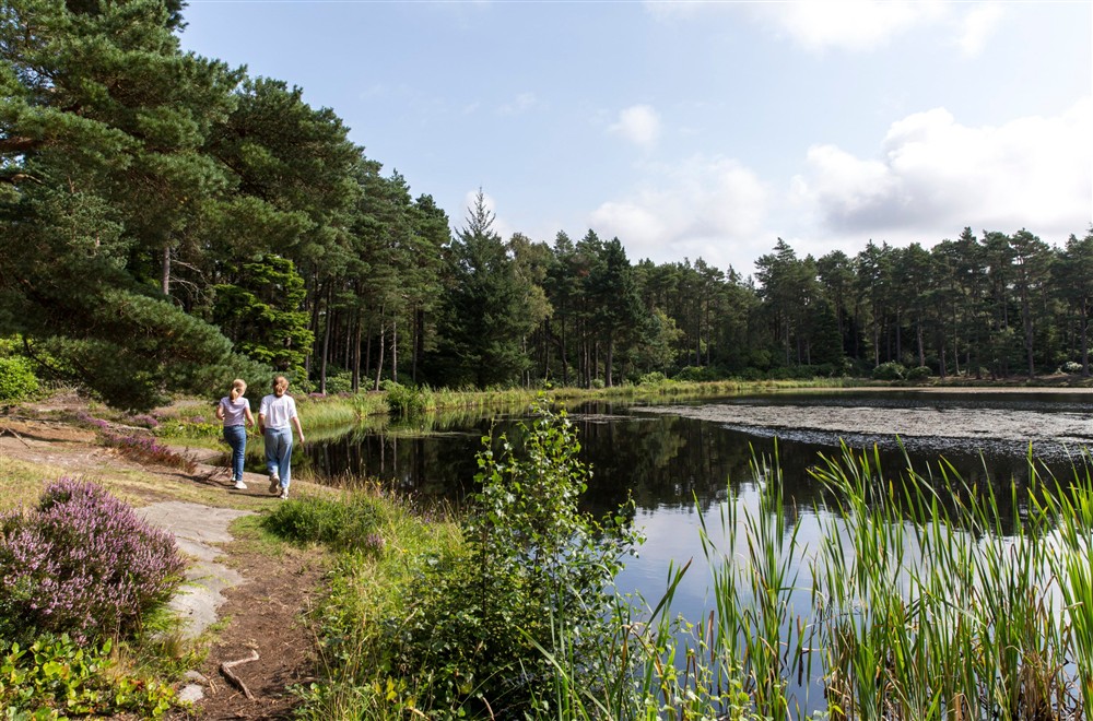 Two girls walking along the banks of the Nellys Moss lakes at Cragside Park Cottage in Rothbury, Northumberland