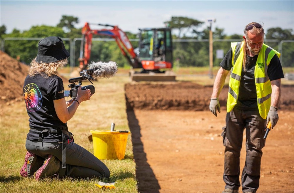 A female camera operator recording an archaeologist at Deben View in Woodbridge, Suffolk