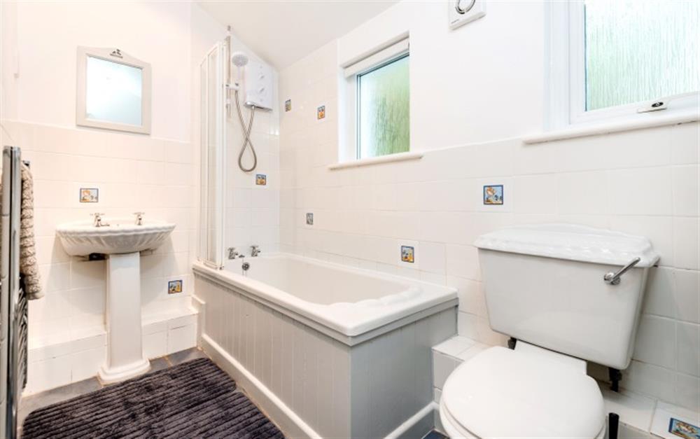 The bathroom, tiled in gleaming white, has both a bath and overhead, electric shower. at Demelza 1 in Helford Passage