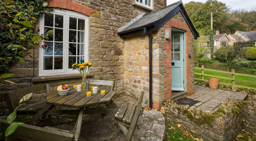 Outdoor table and chairs on the patio at Downhouse Farm Cottage in Bridport, Dorset