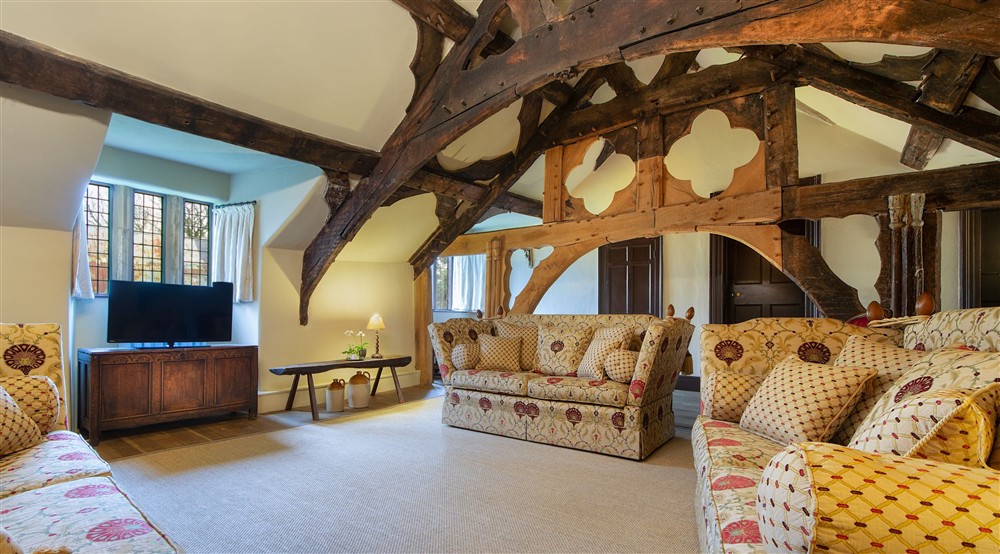 The medieval hall sitting room on the first floor of Egryn. The room has a vaulted ceiling, wooden beams, three sofas, a television and a small dining table, Gwynedd at Egryn in Nr Barmouth, Gwynedd