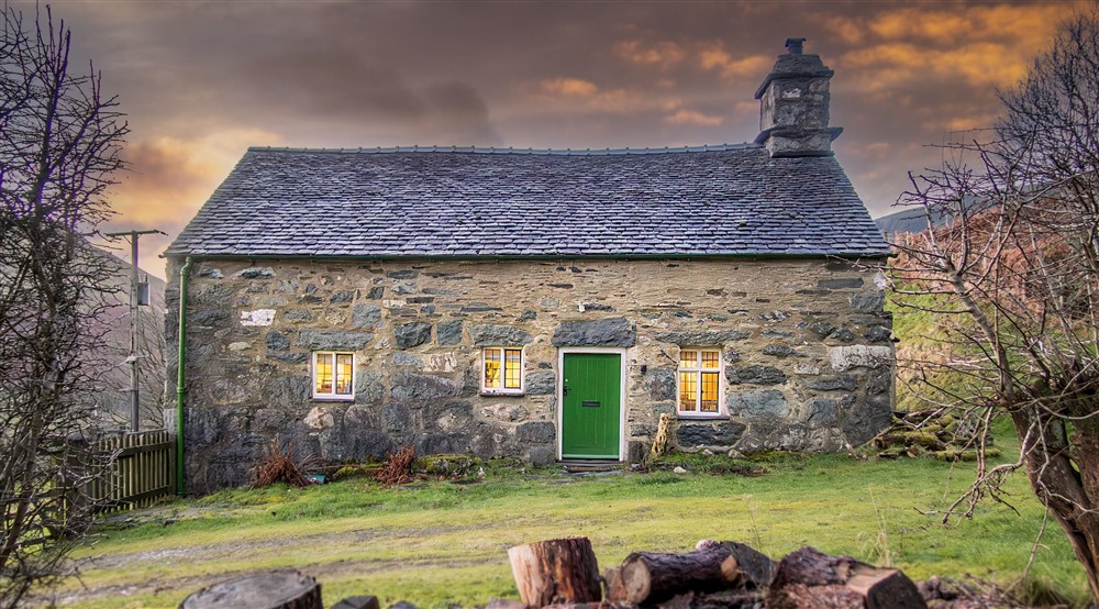 The front of Fron Dirion, a stone cottage, with windows lit up in the evening, Powys at Fron Dirion in Dinas Mawddwy, Powys