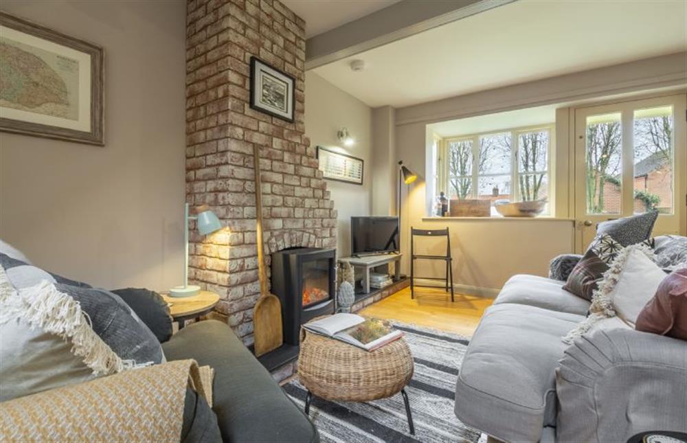 Garden Wall Cottage: Sitting room with large sofa and arm chair around exposed brick fireplace with electric wood burning stove