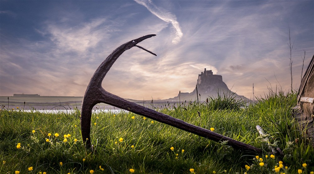 An anchor next to a boat shed on Holy Island, with Lindisfarne Castle in the background, near Glen House, Northumberland at Glen House in Berwick-upon-tweed, Northumberland
