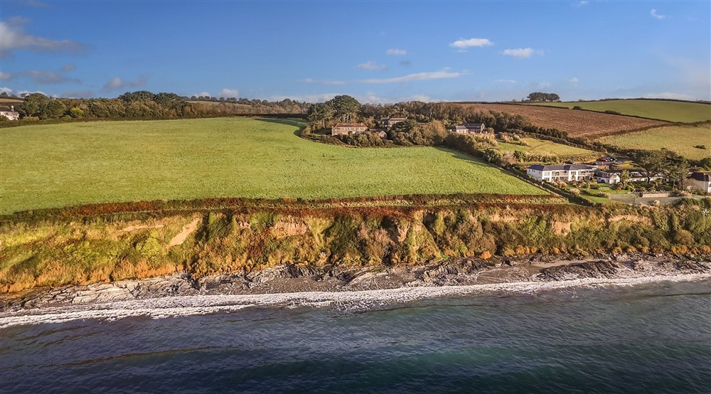 An aerial view of the Gwendra cottages on the cliff above Pendower beach at Gwendra Wartha in Truro, Cornwall
