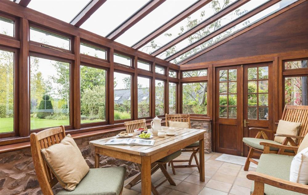 South facing conservatory with table seating six guests and doors to the garden at Hearn Lodge, Bishops Lydeard
