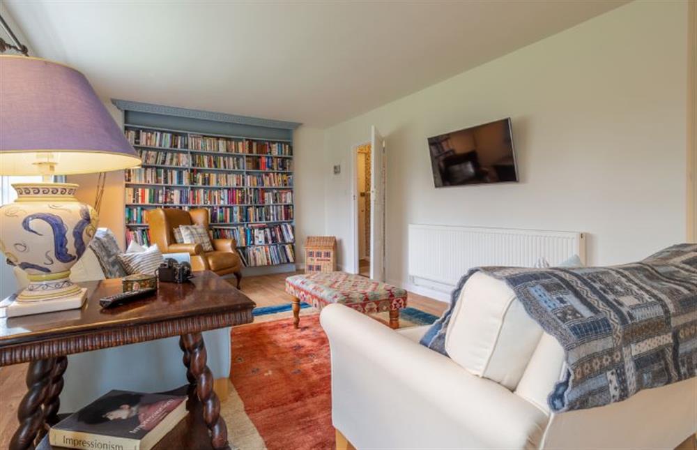 Sitting room with large bookcase and wall-mounted television at Hollyhock Cottage, Stoke By Nayland