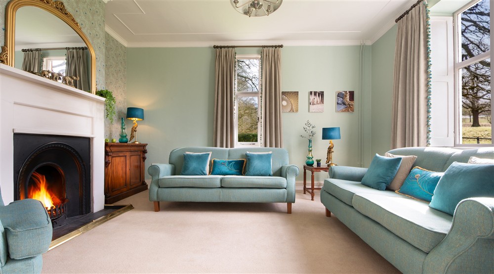The sitting room with sofas, open fire and parkland views at Kedleston Park House in Derby, Derbyshire