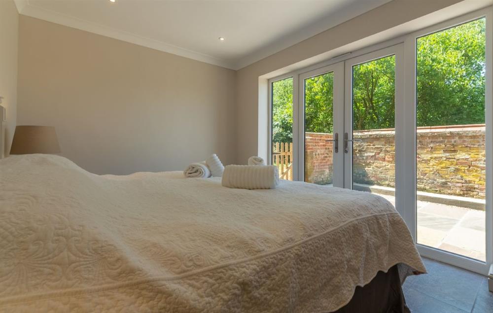 Large bedroom with 6’ super-king size bed and french doors leading out to courtyard at Keepers Cottage, Middleton