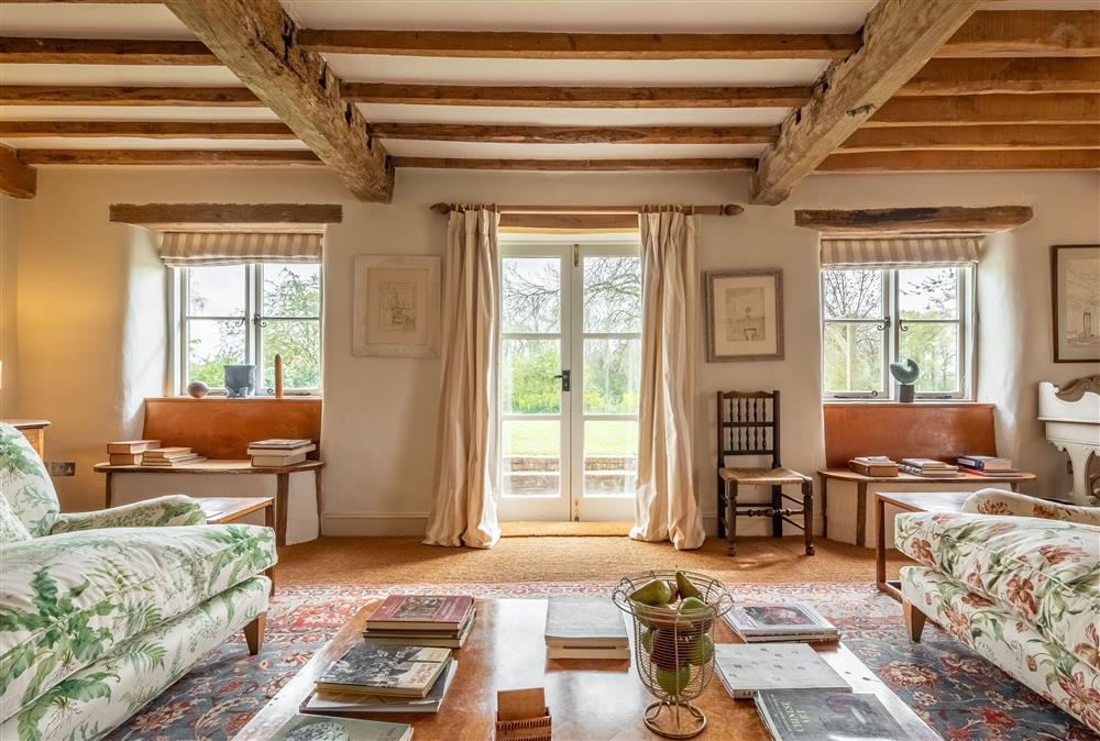 Sitting room with exposed beams running throughout, and french doors leading to the garden at Keepers Cottage, Wolterton