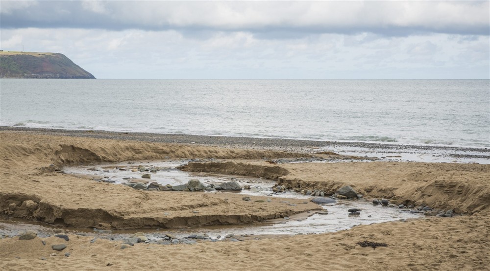 A stream carves its way through the sand towards the sea at Llanborth Farmhouse in Llandysul, Mid Wales
