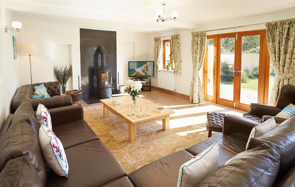 Large sitting room with wood-burning stove and French doors leading out to the large level garden at Long Meadow Barn, Down St Mary