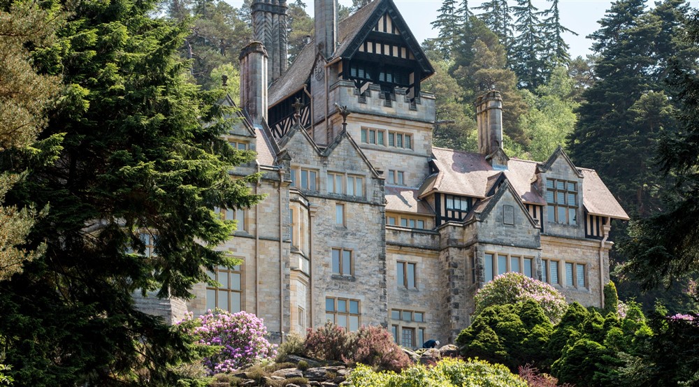 Cragside House on a spring day. The House is surrounded by green trees and there are some flowers appearing in the Rock Garden that surrounded it. at Lookout Cottage in Alnwick, Northumberland