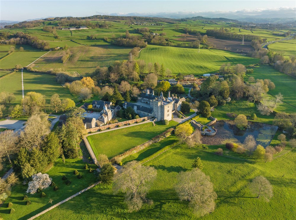 View of Sizerghs grey stone manor house, outbuildings, garden and surrounding estate from above. Its a sunny spring day, and the grass is green. at Low Strawberry Gardens in Nr Hawkshead, Cumbria