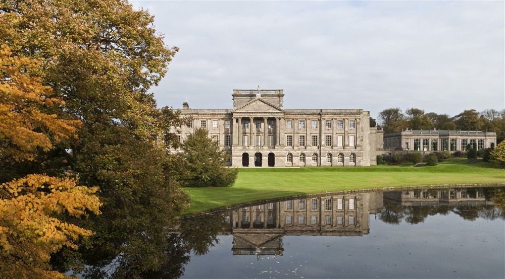 Grand house with columns reflected in a lake and surrounded with autumn trees at Lyme West Lodge in Macclesfield, Cheshire