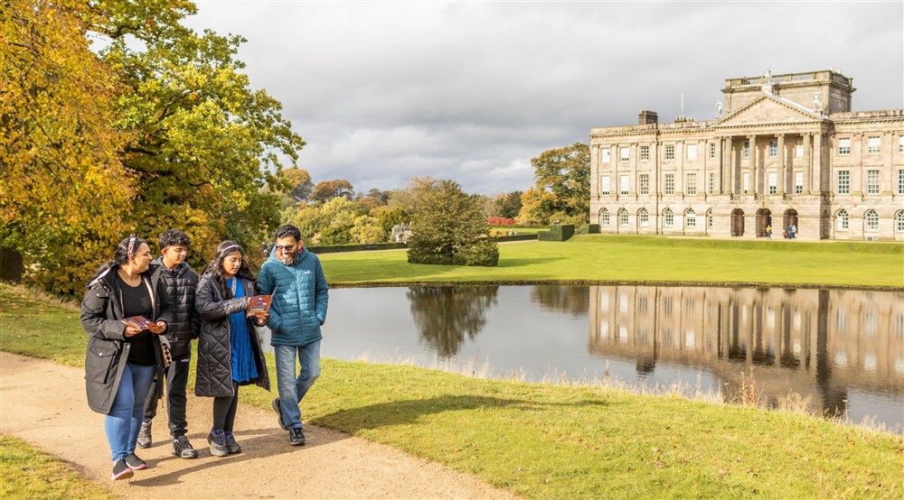 Visitors exploring the garden on a family trail, with a lake and the house in the background in Autumn at Lyme West Lodge in Macclesfield, Cheshire