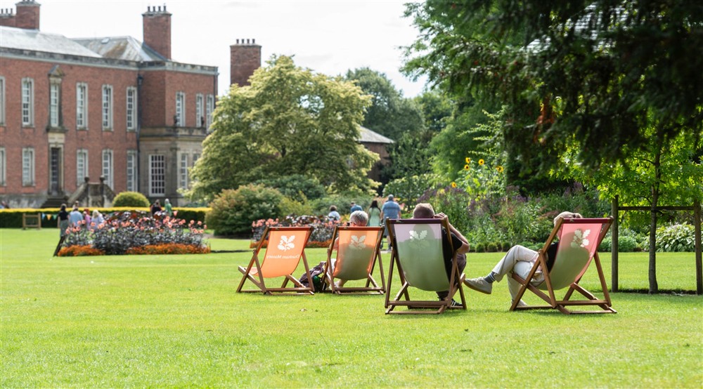 Visitors sat on deckchairs on the lawn, a historic house in the background. at Lyme West Lodge in Macclesfield, Cheshire