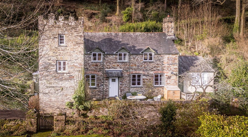 An aerial view of the exterior of Malt House, a stone cottage with a small tower, patio for outdoor dining and private garden, Cornwall at Malt House in Saltash, Cornwall