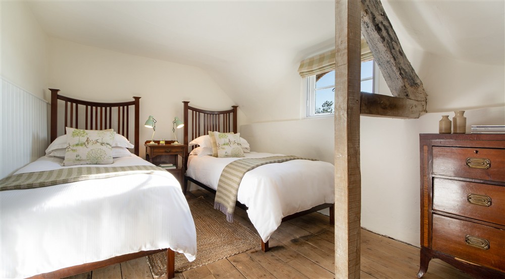 The twin bedroom, with sloped ceiling and original beams, at Middlebere Farmhouse in Isle Of Purbeck, Dorset