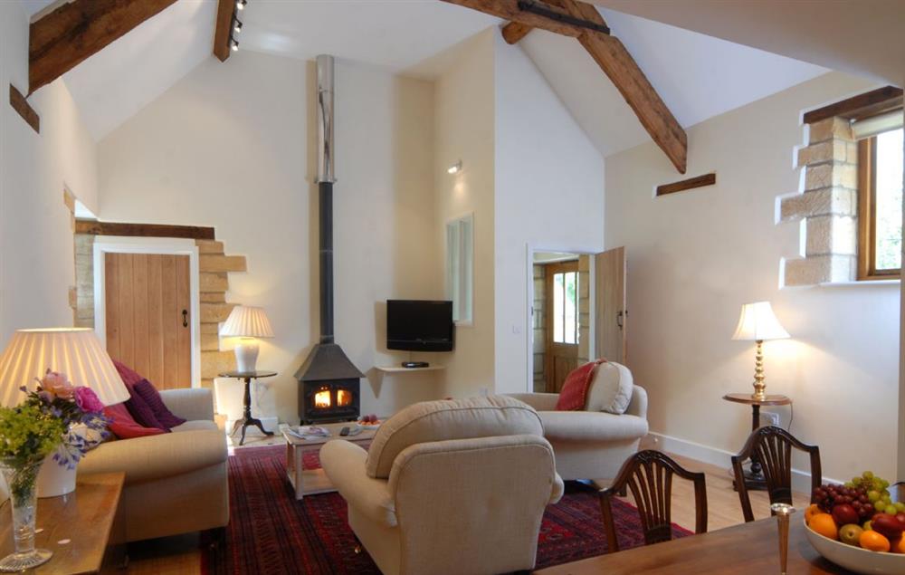 Sitting room with wood burning stove and exposed beams at Nellies Barn, Naunton