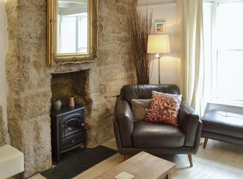 The living room features a stone fireplace and electric woodburner at Oaken Cottage in Mousehole, Penzance, Cornwall., Great Britain
