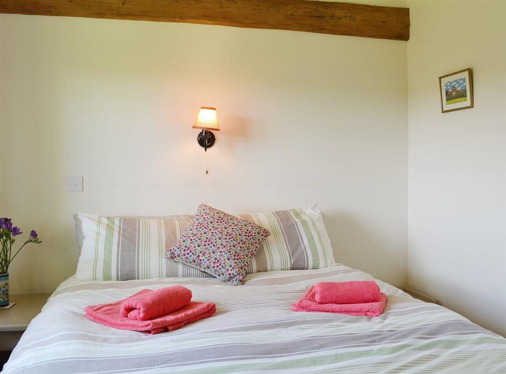 The double bedroom has a kingsize bed and rustic exposed woodwork at Old Dairy Barn in Playden, near Rye, East Sussex