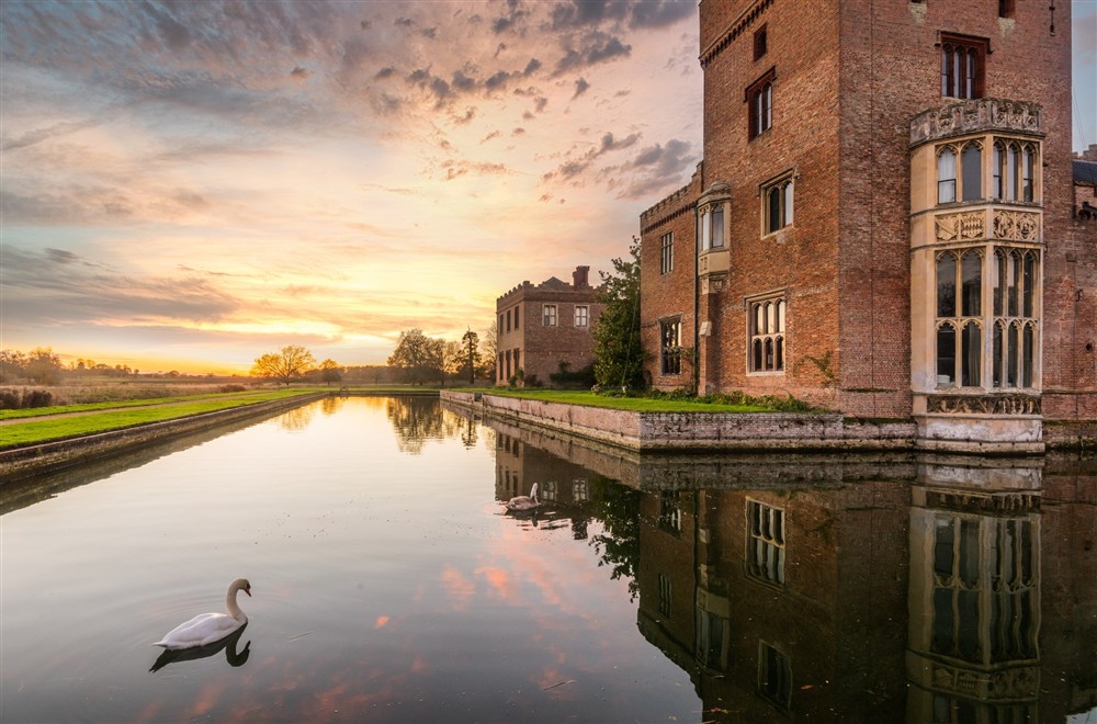 A swan is swimming on the moat surrounding Oxburgh Hall at Peckover Stable Lodge in Wisbech, Cambridgeshire