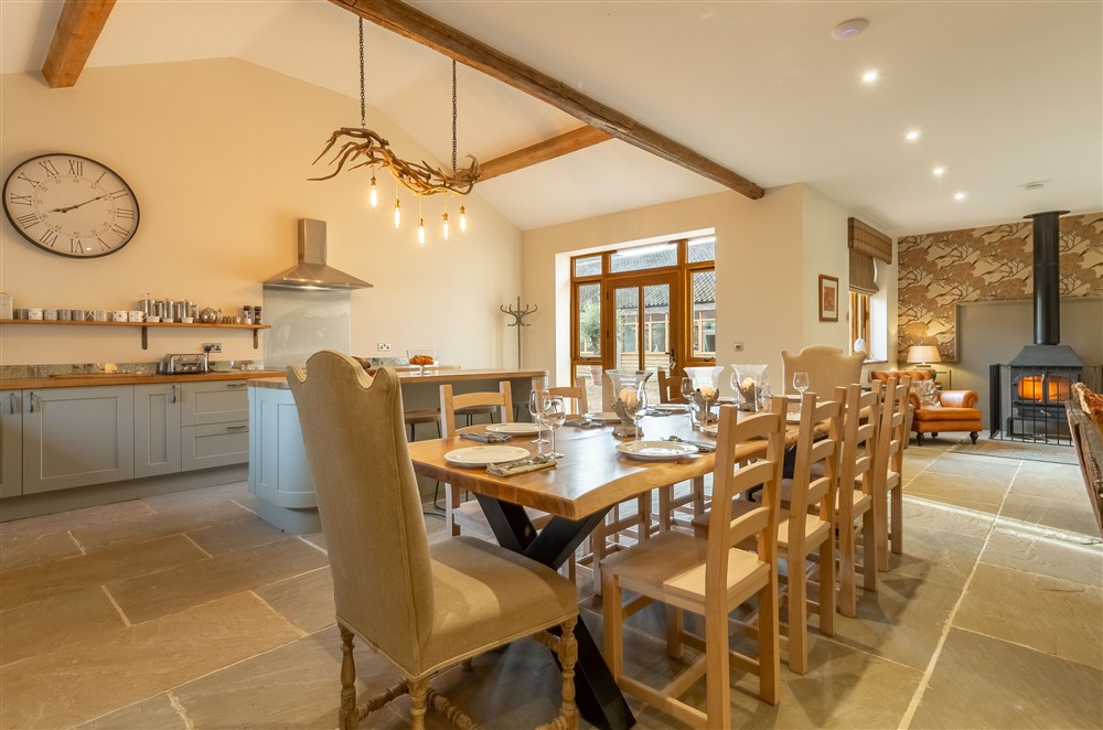 Kitchen/ dining/ sitting area with hand-made dining table, antler chandelier, large leather sofas and wood burning stove