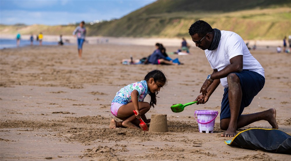 Father and daughter building a sandcastle on the beach in summer at Rhossili Old Rectory in Rhossili, South Wales