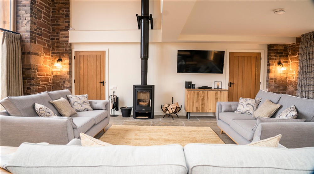 The sitting area in the open-plan living space of Sandybury Barn, with three sofas, television, woodburner and a vaulted ceiling, Shropshire at Sandybury Barn in Bridgnorth, Shropshire
