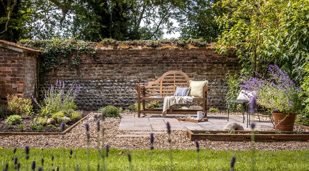 A patio area and bench, surrounded by flower beds and lawn in the garden at Sexton's Lodge in Norwich, Norfolk