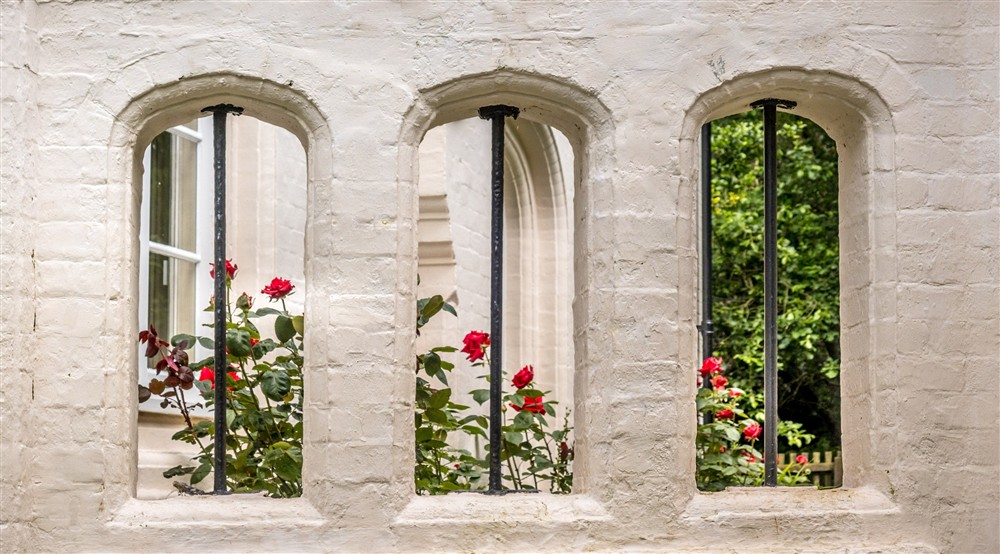 Roses through the arches in the garden wall of Sextons Lodge, Norfolk at Sexton's Lodge in Norwich, Norfolk