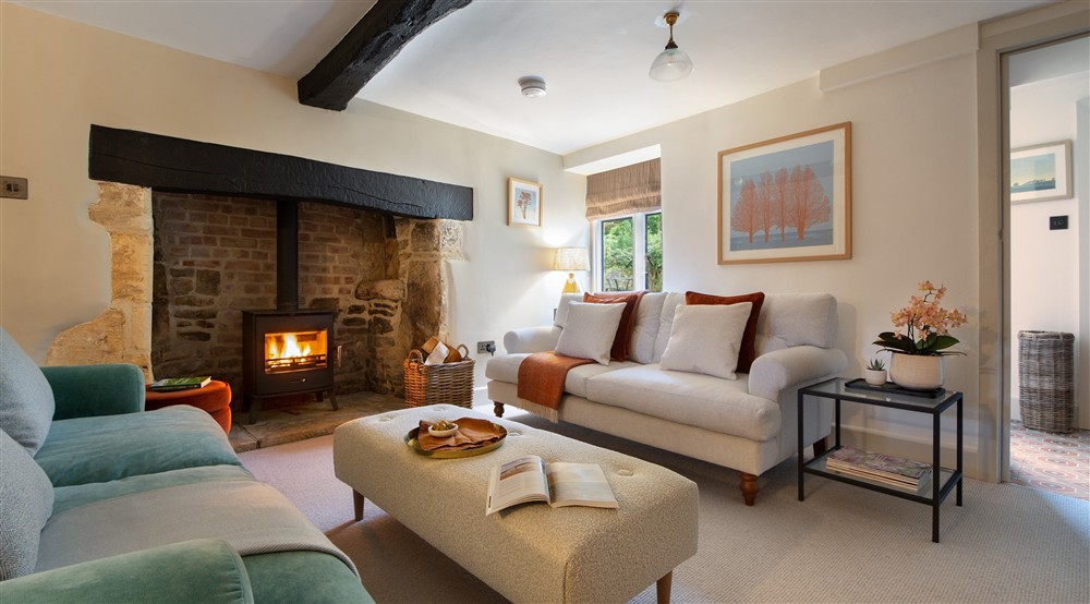 The open-plan sitting and dining room, with original beams and inglenook, and woodburner at Sherborne West Lodge in Sherborne, Gloucestershire