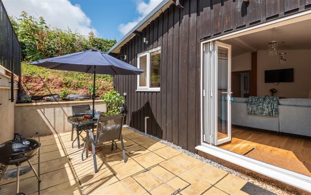 Bifold doors lead to the lower terrace with table and chairs and a  charcoal barbecue for al fresco dining at Stable Barn in Slapton