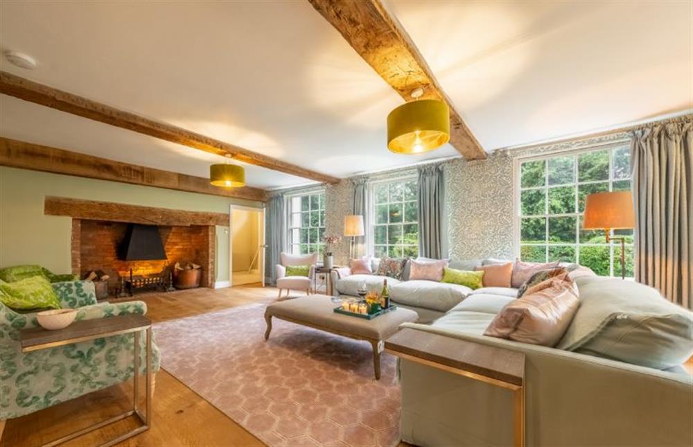 Drawing room with exposed beams and large windows overlooking the garden at The Farmhouse, Nether Hall Estate, Pakenham