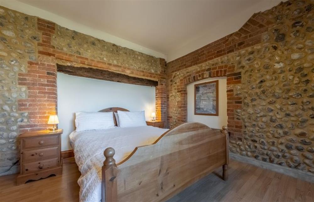Master bedroom with exposed flint walls and a king-size bed at The Felmingham, Roughton near Norwich